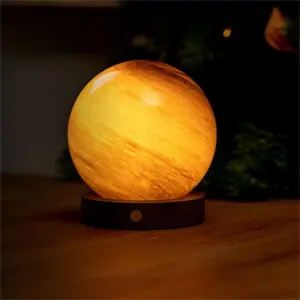 Kugleformet lampe med varm glød, marmoreret tekstur og cirkulær base på bordet.