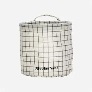 Beige opbevaringskurv med grå tern, håndtag og teksten "Nicolas Vahé" på forsiden.