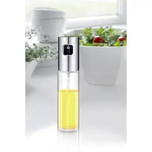 Klar olie sprayflaske med gul olie, stående på køkkenbord med salat i baggrunden.