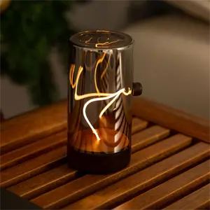 Cylindrisk bordlampe i reflekterende metal med dekorativ lysfilament på træoverflade.