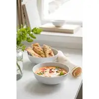 To skåle, én med suppe og én med frituremad, står på en lys overflade nær et vindue.