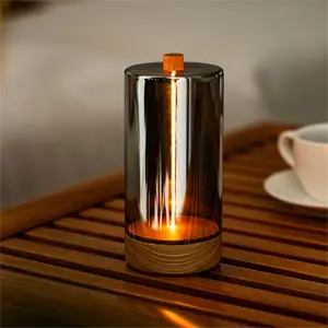 Cylinderformet bordlampe med reflekterende overflade, træbase og varm glød på en træbord.