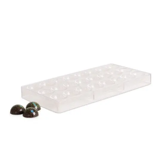 Klar plastform til halvkugler med tre dekorerede chokolader ved siden af.