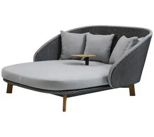 Udendørs daybed med grå vævede sider, lysegrå hynder, tre puder og et lille bord i midten.