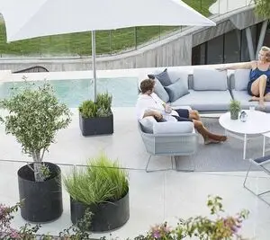Terrasse med parasolfod og plantekasse på hjul, grå møbler ved pool, moderne udendørs design.