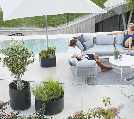 Terrasse med parasolfod og plantekasse på hjul, grå møbler ved pool, moderne udendørs design.