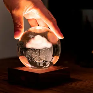 Hånd rører ved kugleformet lampe på træbase med 3D laserindgraveret sky og regn.