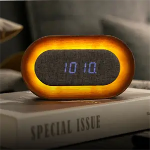 Oval vækkeur med blå digital skærm "10:10" og varm lysring, placeret på en bog i hyggelig atmosfære.