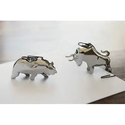 To skinnende figurer, en tyr og en bjørn, med papirclips på, står på en overflade.