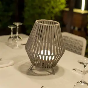Dekorativ lanterne med geometrisk design på bord, lys indeni, omgivet af vinglas og stol.