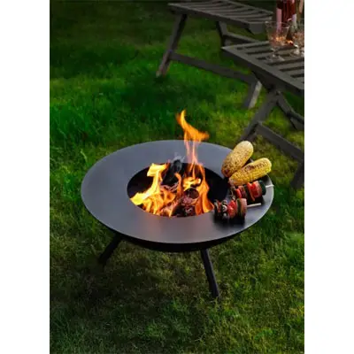 Rundt bålsted på græs med flammer, majs og spyd til grill. Stole og bord i baggrunden.