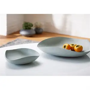 To lysegrønne skåle, minimalistisk design, den ene større med frugt, på hvid overflade.