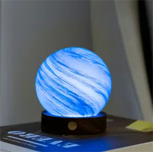 Lille kuglelampe med blå-hvidt marmormønster, udsender blødt lys på mørk base, står på bog.