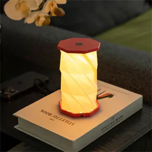 Kompakt koralrød hexagonlampe med snoet, lysende design, placeret på en bog i et hyggeligt rum.