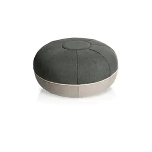 Rund pouf i stålgrå med mørk top, lysere base og synlige sømme fra midten.