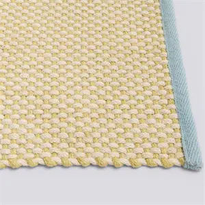 Tæppe i blød gul med blå kant og tydelig vævet tekstur.