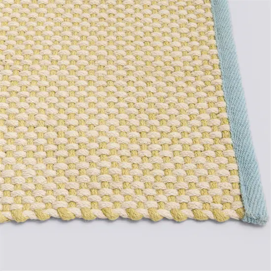 Vævet tæppe i gule og beige nuancer med lys blå kant og tæt, regelmæssigt mønster.