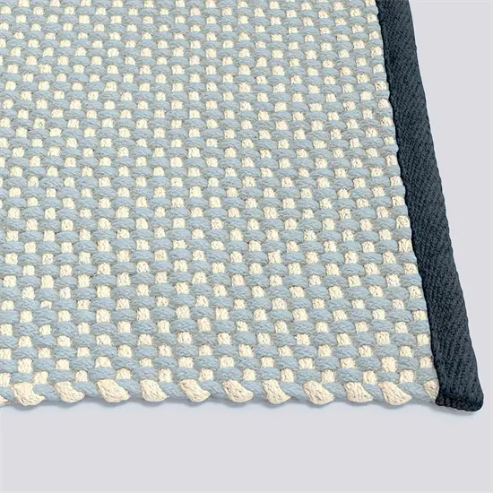 Tæppe med vævet mønster i blød turkis og lysere nuancer, kantet med mørkere turkis/grå farve.