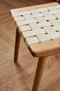 Taburet med vævet sæde af lyse stropper, fire lyse træben i minimalistisk stil.