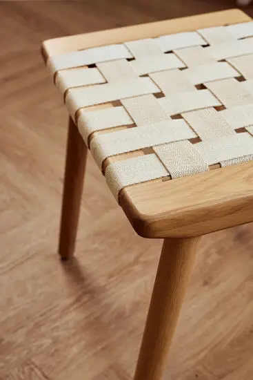 Taburet med vævet sæde af lyse stropper, fire lyse træben i minimalistisk stil.