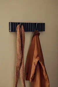 Moderne vægmonteret knagerække med vipbare kroge, der holder en brun jakke og et tørklæde.