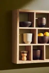 Vægmonteret hylde i eg med gitterdesign, indeholder skåle, kopper, citroner og lille emblem på siden.