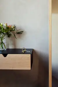 Sort hylde med lys træskuffe, vase med blomster og nøgler ovenpå.