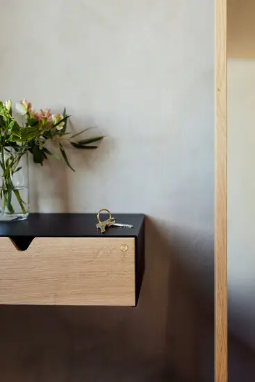 Sort hylde med lys træskuffe, vase med blomster og nøgler ovenpå.