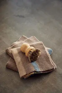 Strikket karklud i beige og blå med label i hjørnet. En træbørste ligger ovenpå kluden.