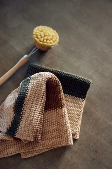 Strikkede karklude med striber i grøn og brun, liggende ved siden af en træbørste på en overflade.