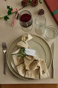 Grønstribet serviet med logo på tallerken, pyntet med kortholder, bestik og juledekorationer.