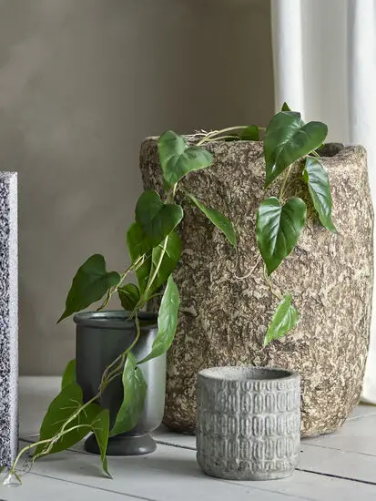 Kunstig plante med grønne, hjerteformede blade i stor, tekstureret potte på gulvet.