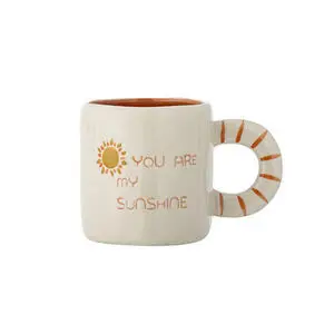 Lys krus med tekst "YOU ARE MY SUNSHINE", solillustration og orange stribet hank.