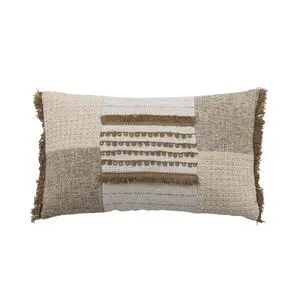 Rektangulær pude med patchwork-design i naturfarver, teksturer og frynser langs kanterne.