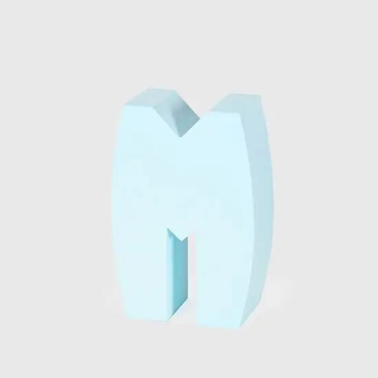 Lyseblåt, tredimensionelt bogstav "M" med glat overflade, stående oprejst på lys baggrund.