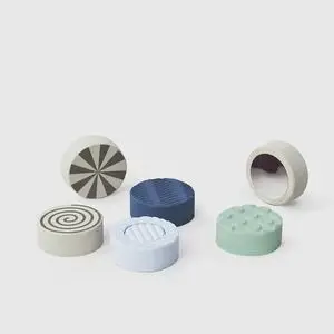 Seks runde sten med spiraler, riller og knopper i blå, grøn og beige.