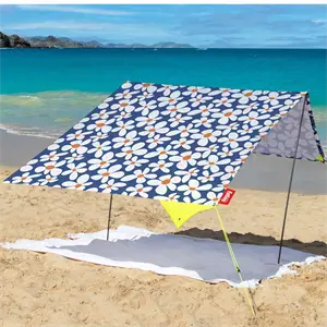 Bærbart strandtelt med blomster på sandstrand, udsigt til havet. Holdes oppe af to stænger og snore.