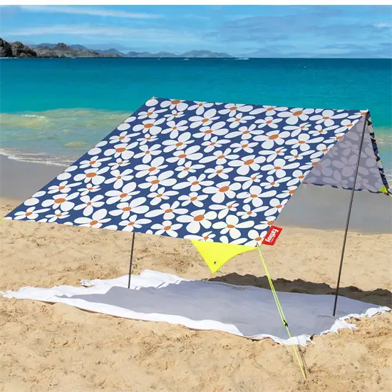 Bærbart strandtelt med blomster på sandstrand, udsigt til havet. Holdes oppe af to stænger og snore.