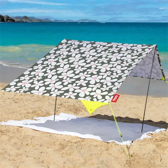 Bærbart strandtelt med blomstermønster opsat på sandstrand ved havet, giver skygge.