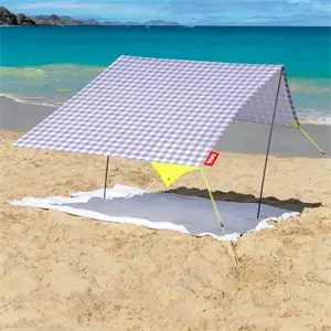 Bærbart strandtelt med lilla/hvidt ternet mønster, opsat på en strand med udsigt til havet.