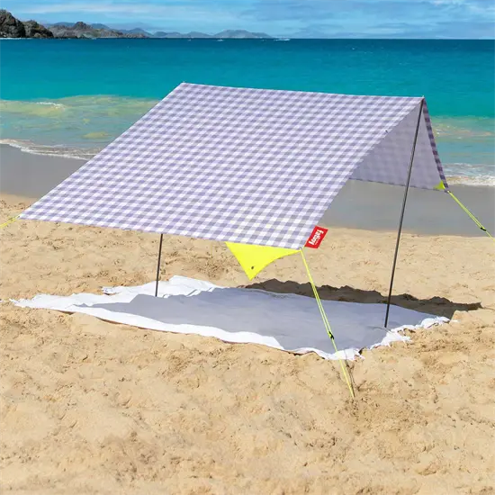 Bærbart strandtelt med lilla/hvidt ternet mønster, opsat på en strand med udsigt til havet.