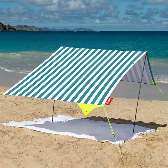 Strandtelt med hvid/turkis striber på sandstrand, hav i baggrunden. Triangulær form, lette stænger.