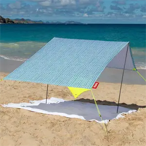 Bærbart strandtelt i hvid og turkis tern på sandstrand med hav og himmel i baggrunden.