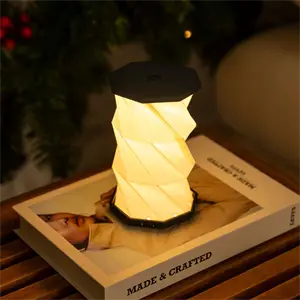 Lille bordlampe med hexagonal top og snoet design, udsender varmt lys, står på en bog.