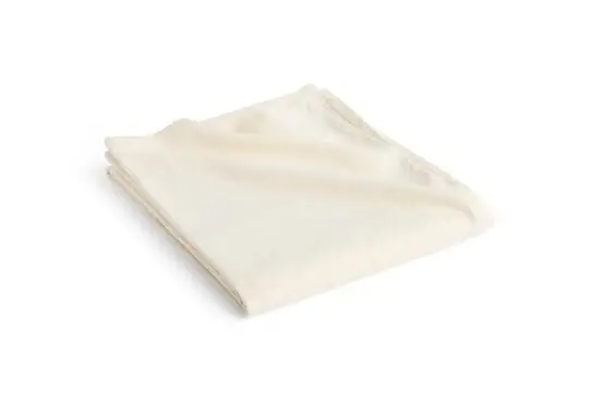 En cremefarvet sengetæppe i hør, foldet pænt. Stoffet ser blødt og let ud med en glat overflade.