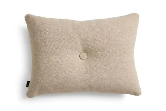 Rektangulær beige pude med tekstur, central knap, afrundede kanter og Hay-mærke på siden.