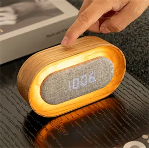 Ovalt vækkeur med lysende kant, tekstilfront og digitale tal, der vises som 10:06.