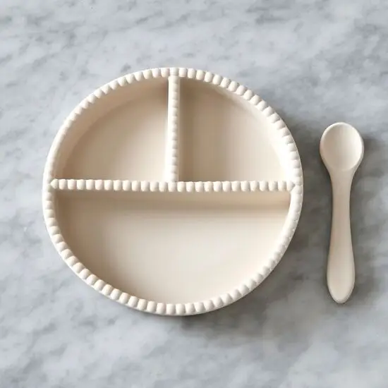 Flødefarvet børnesæt med opdelt tallerken og matchende ske til portionering af mad.