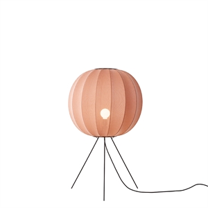 Rund koralfarvet lampe med stribet skygge, tre ben og synlig ledning. Lys ses gennem hul i midten.