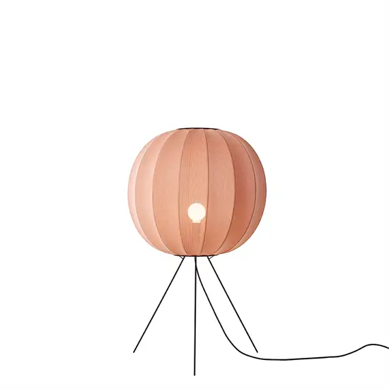 Rund koralfarvet lampe med stribet skygge, tre ben og synlig ledning. Lys ses gennem hul i midten.